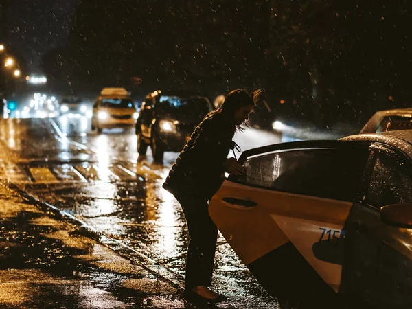 Moskou. Rusland. 17 september 2020. Silhouet van een vrouw in de koplampen van auto 's die de taxideur openen. — Stockfoto