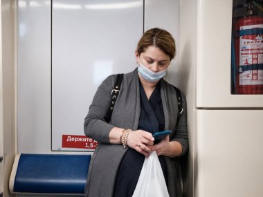 Moskova. - Rusya. 5 Ekim 2020 'de metro vagonunda koruyucu maskeli genç bir kadın akıllı telefon tutuyor..