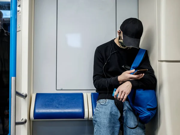 Ein Mann in einem U-Bahn-Wagen blickt begeistert auf sein Smartphone. Der Passagier hat eine medizinische Schutzmaske auf dem Gesicht. — Stockfoto