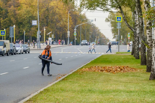 Moszkva. Oroszország. Október 11, 2020 Egy női közműmunkás használ fúvót, hogy távolítsa el a lehullott levelek egy város utcájában. — Stock Fotó