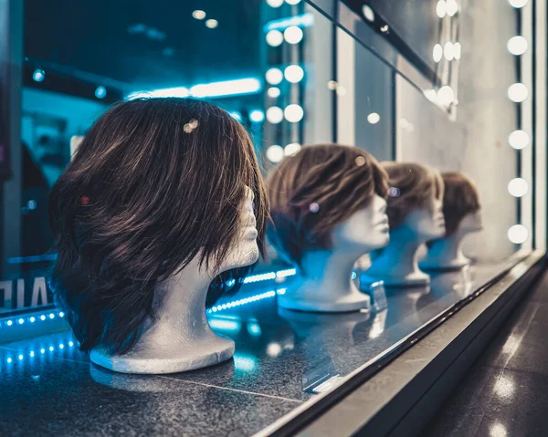 Cabeças femininas de manequins sucessivamente em uma janela de loja à noite. Luzes de néon azul e branco e brilho em vidro. — Fotografia de Stock