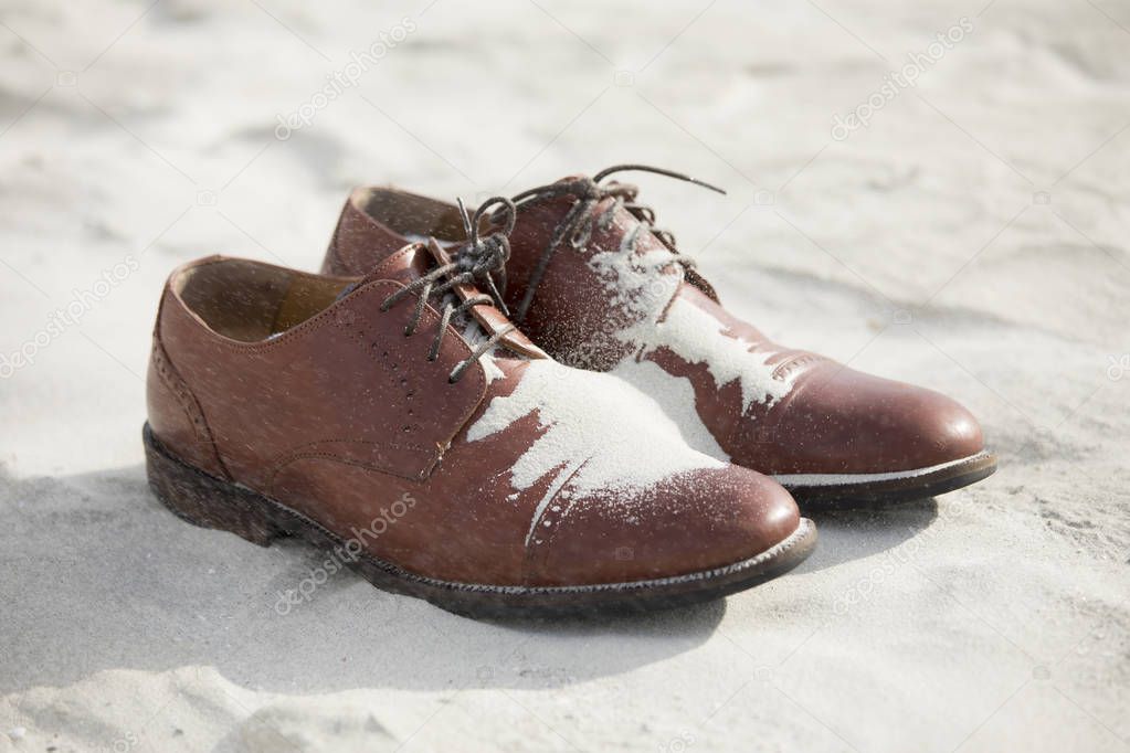 Dress shoes for groom on the beach with blowing sand.