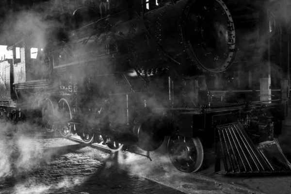Steam locomotive at train station with dramatic lighting and steam