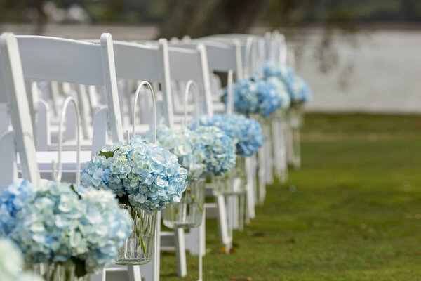 Bouquets of hydrangeas hanging from chairs for outdoor wedding.