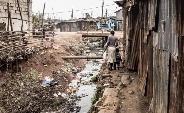 Menschen gehen in einem Slum in Afrika an einer offenen Kanalisation entlang — Stockfoto