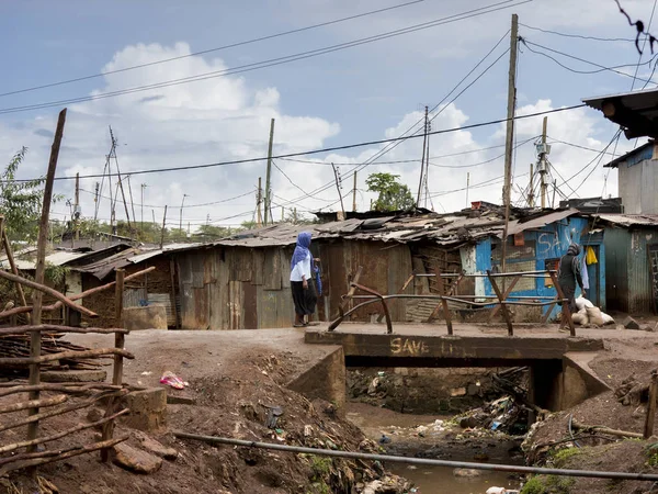 Pessoas andando ao longo de um esgoto aberto em uma favela na África — Fotografia de Stock