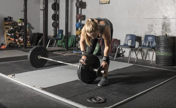 Strong young female weight lifter loading weights onto barbell i — Stock Photo, Image