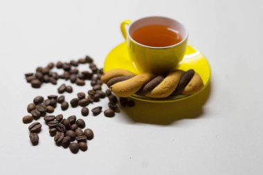 Sarı kupa çay, kahve taneleri ve kurabiyeler.