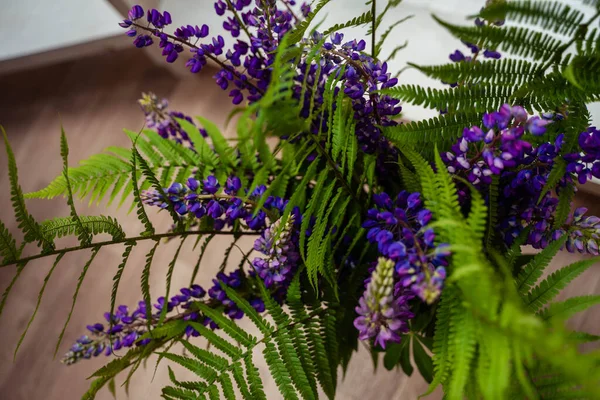 a bouquet of lupins and fern stands in a vase
