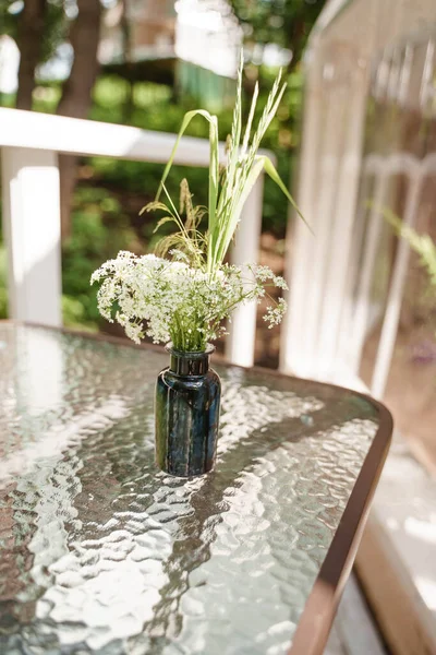 Skleněná váza stojí na průhledném stole s květinami — Stock fotografie
