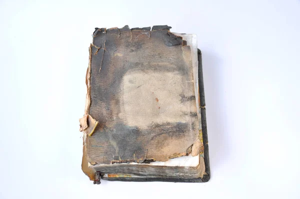 An old burnt book with a torn cover is lying on the table on a white background.