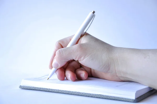 man\'s hand holding a pen and writing in a notebook