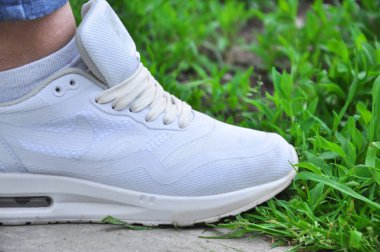 Beyaz spor ayakkabılar yeşil çimlerin yanında betonun üzerinde duruyor.