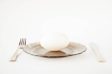 Tabakta büyük bir kaz yumurtası var. Bıçak ve çatalın yanında beyaz bir arka plan üzerinde masanın üzerinde