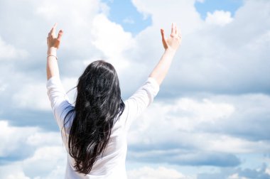 A woman with her hands up on a green field praises God. Prayer with arms raised. Blue sky and white clouds.... clipart