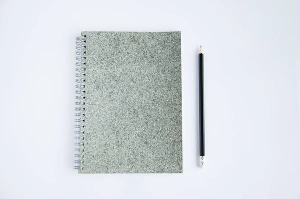 a gray notebook lies on the table. On the pad or near it is a black pencil. On a white background