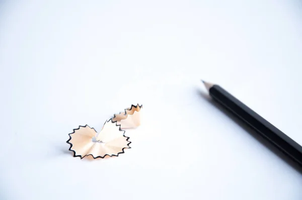 black pencil lies on the table. Nearby is shavings from a pencil. On a white background