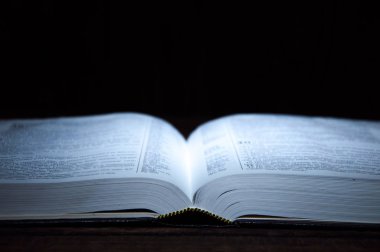 karanlıkta masanın üzerinde yatan açık kitap. Kitap Üzerinde Işık