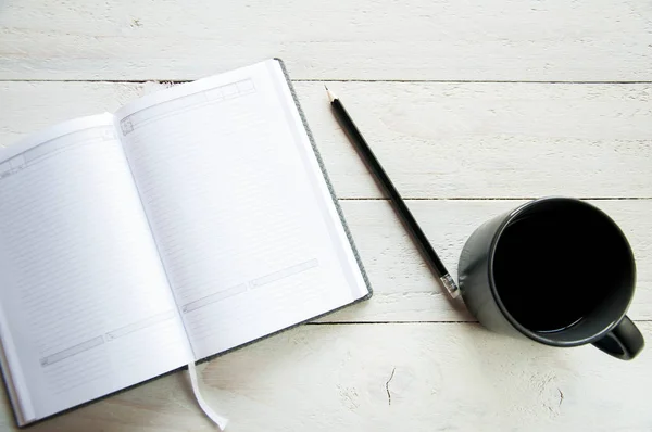 一个带咖啡的黑杯子和一张白桌上的开放式笔记本 白色木制背景 董事会 — 图库照片