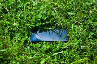 Siyah cep telefonu yeşil çimenlerde yatıyor. Yaz