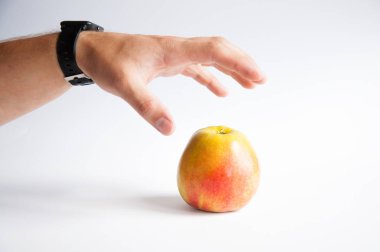 Bir elma beyaz bir arka plan üzerinde beyaz bir masa üzerinde duruyor. El elma alır