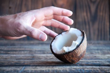 Eli ahşap bir masanın üzerinde duran yarım hindistan cevizini alır. Beyaz posa ve hindistan cevizi kabuğu