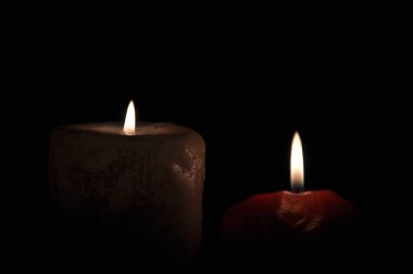 Karanlıkta iki büyük mum yanıyor. Siyah bir arkaplanda