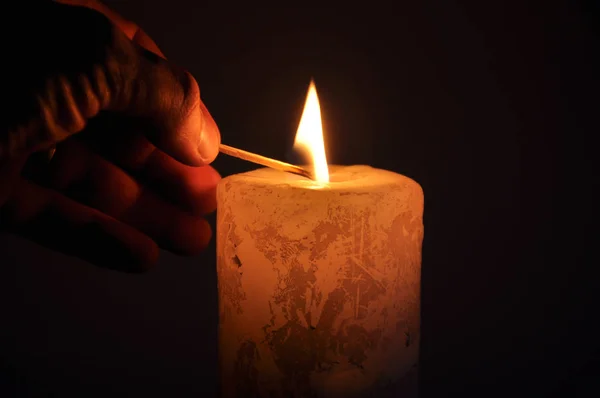 一个点燃的火柴在手 点燃一支大蜡烛 在黑色背景上 — 图库照片
