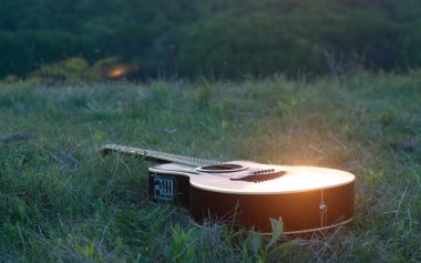 Gitar çimlerin üzerinde yatıyor. Gün batımı güneşi. Yaz
