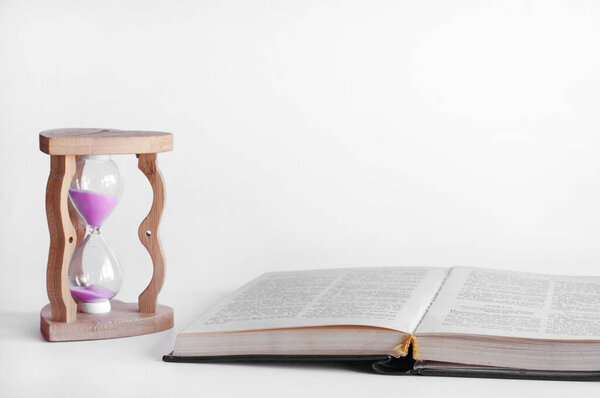 Hourglass and open bible book. On a white background