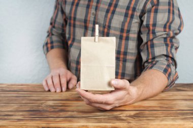 Genç bir adam elinde bir kese kağıdı tutuyor. Hediye. Tahta bir masada oturuyor.