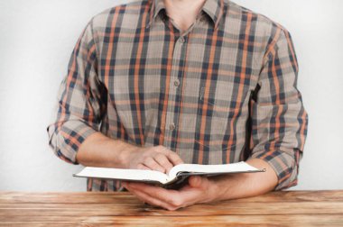 İncil 'i bir adamın elinde açmak. Tahta bir masada oturuyor.