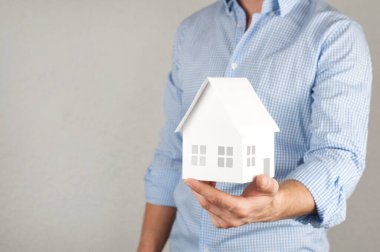 Gömlekli bir adam minyatür bir ev tutuyor. İşadamı