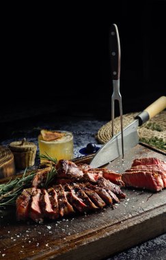 Büyük bir parça pişmiş ve dilimlenmiş biftek. Tahtada, bıçakla ve bir kokteyl ile servis ediliyor.