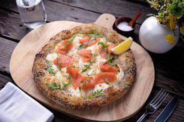 Krema bazlı füme somon pizzası ve ahşap bir tahtada servis edilen otlar.