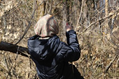Parlak güneşli bir günde eriyen kar ve kadın siyah ceket, şal, halat üzerinde sallanan kırmızı çivi ile erken bahar ormanı