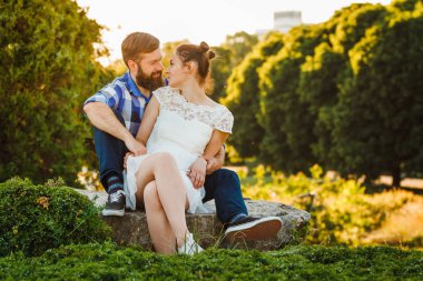Mutlu romantik çift kucaklama taşlar üzerinde oturur ve onlar birbirlerine bakıyorlar. Sevimli küçük kız ve acımasız sakallı adam açık.