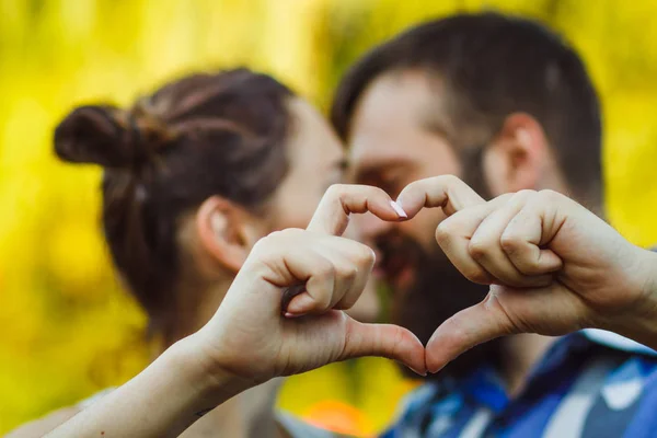 Couple in love gesturing heart with fingers. Portrait of brunette and her handsome bearded boyfriend in park