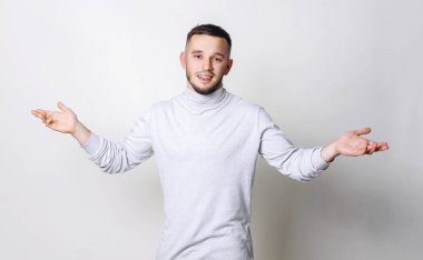 Beyaz boğazlı kazak yükseltir elinde sürpriz söyleyerek genç adam ayakta veya gri arka plan kopya alanı biriyle hoş geldiniz