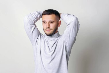 Yakışıklı adam kafasını tutarak. Beyaz boğazlı kazak erkekte el ele tutuşsun başını ve sıkıştırılmış dudaklar için bir gri arka plan kopya alanı