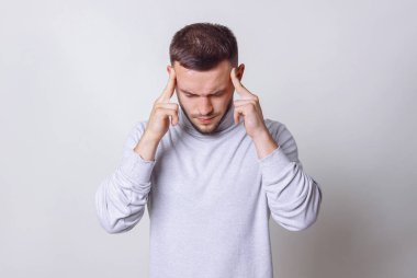 Çok yoğun bir şekilde having baş ağrısı portre portre adam olduğunu düşünüyor. Beyaz boğazlı kazak insani duygular adam alnına parmaklarıyla dokunur. Alan gri arka plan kopyalama