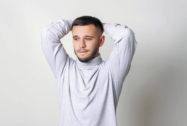 Handsome man holding his head. Man in white turtleneck hold hands to his head and compressed lips on a gray background copy space