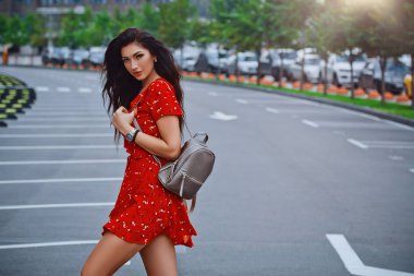 Genç esmer kız ayakta ve pozlar kırmızı arka plan üzerinde yer Park şehir sokakta Omzunda sırt çantası ile kısa elbise giyer