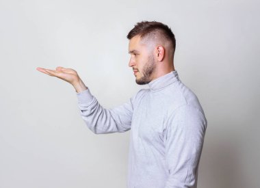 Profil portre yakışıklı bir adam bir şey bir gri arka plan kopya alanı elinde avuç gösterilen