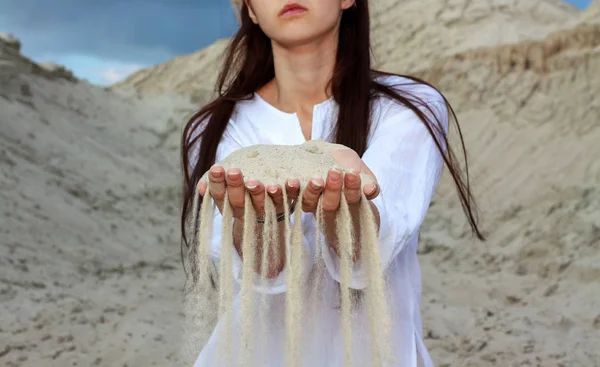 Sand in hands of girl. Cute brunette woman in a white blouse sand running through hands as a symbol for time running, lost