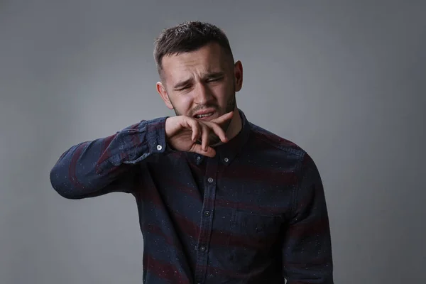 Young guy wipes mouth and lips with sleeve. Man with beard in checkered shirt facial expression. Dark gray background copy space