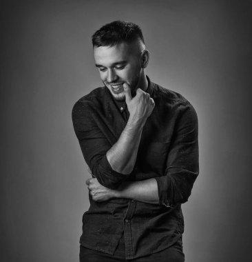 Gri arka plandaki yakışıklı genç adam kameraya bakıyor. Gri duvara yaslanmış elleri ceplerinde gülen genç adamın portresi. Mutlu adam gülümsüyor.