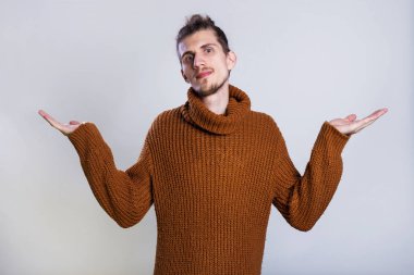 Genç adam el avuç içi kadar gösteri yükseltir ya da bir şey gösteren gri arka plan kopya alanı üzerinde sıcak örme kazak giymiş.