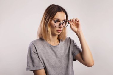 Sarışın kadın kadının gri arka plan üzerinde poz onun gözlük dokunmadan büyük yuvarlak gözlük takıyor yan isteyen Studio vurdu