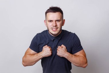 Genç kızgın kaslı adam kenetlenmesi diş gösterir sırıtarak siyah gömlek, göğsüne yakın kapalı yumruklarını izole gri arka plan üzerinde.